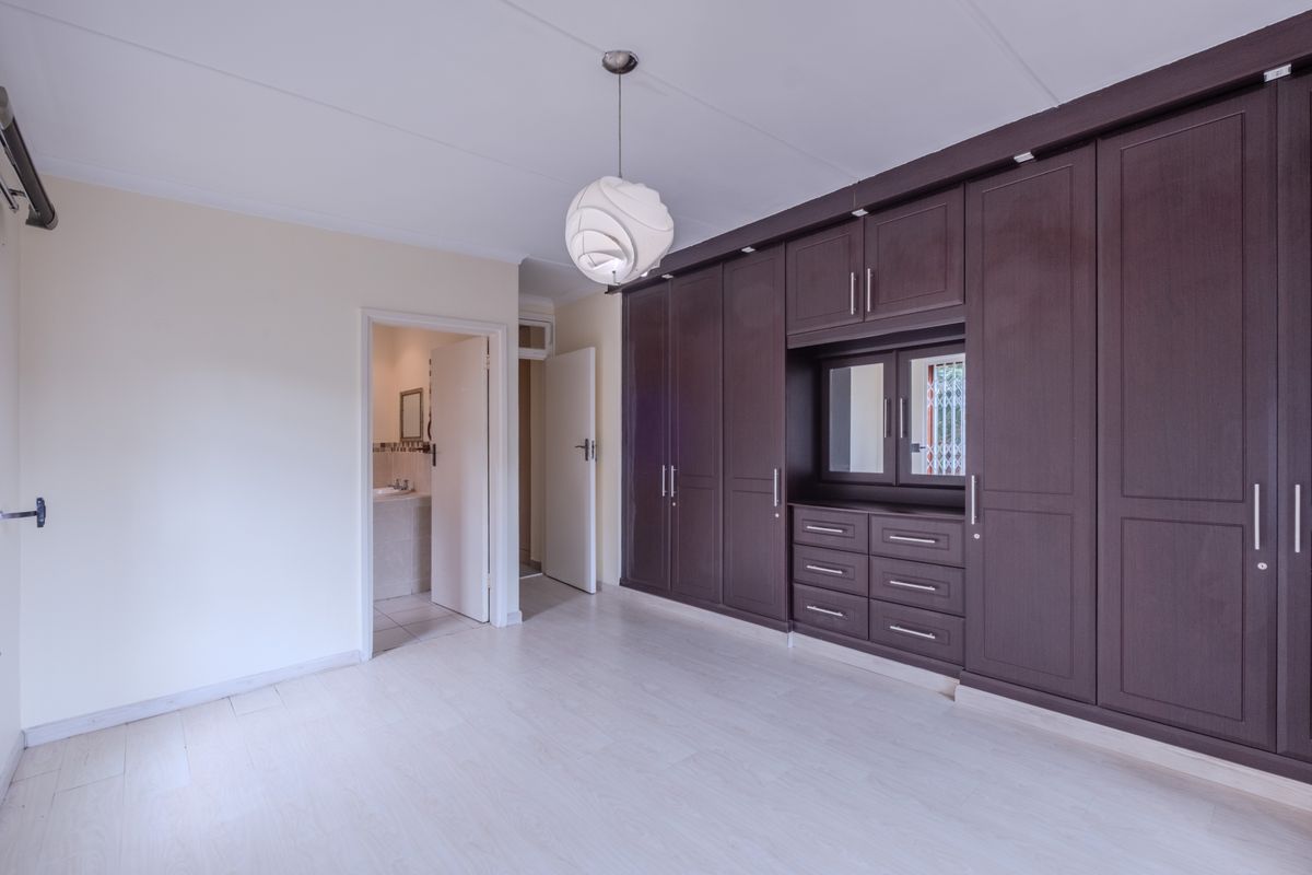 Spacious bedroom featuring extensive dark wood built-in cupboards, light laminate flooring, and direct access to an en-suite bathroom.