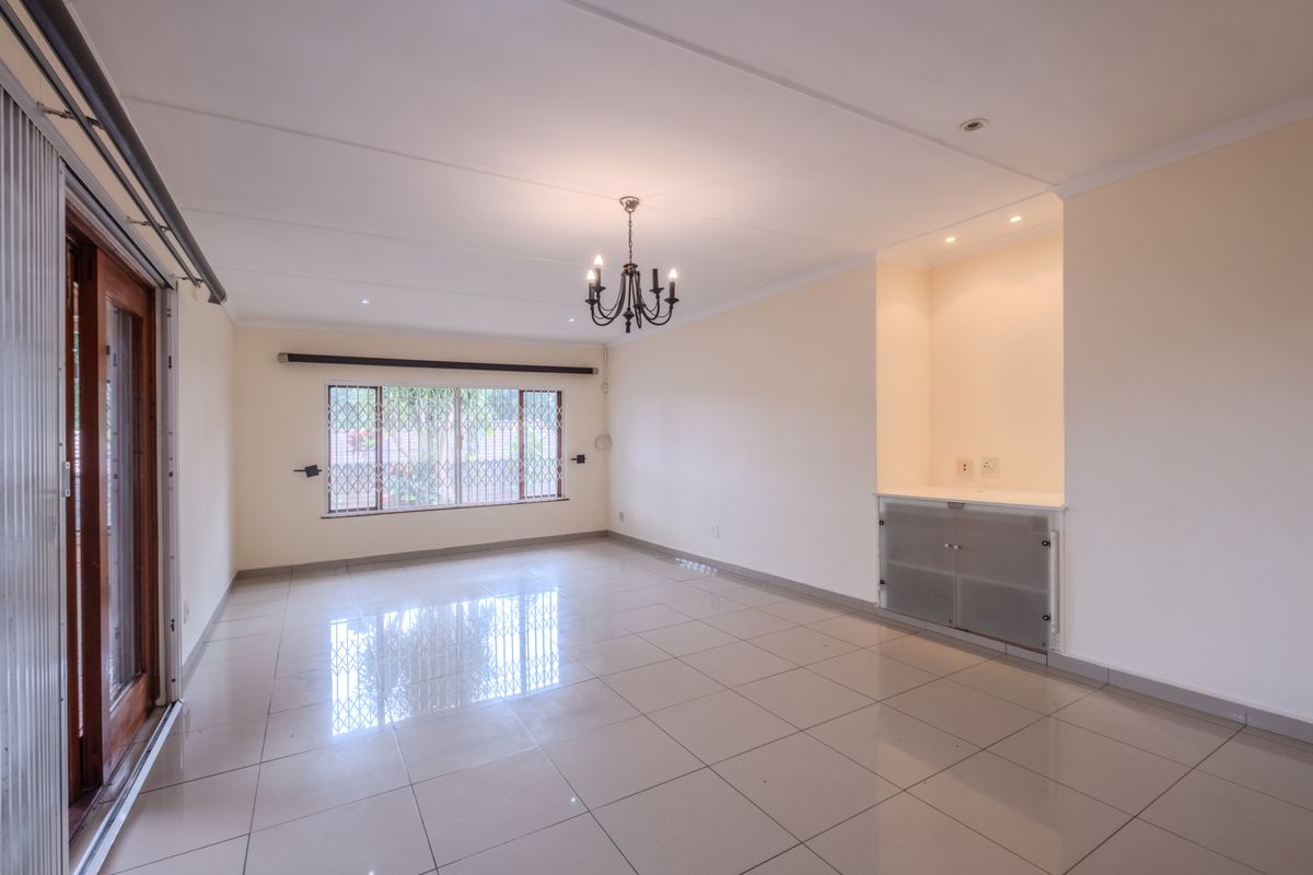 A spacious, light-filled living area featuring polished tiled floors, a classic chandelier, and built-in cabinetry, offering a clean and versatile space.