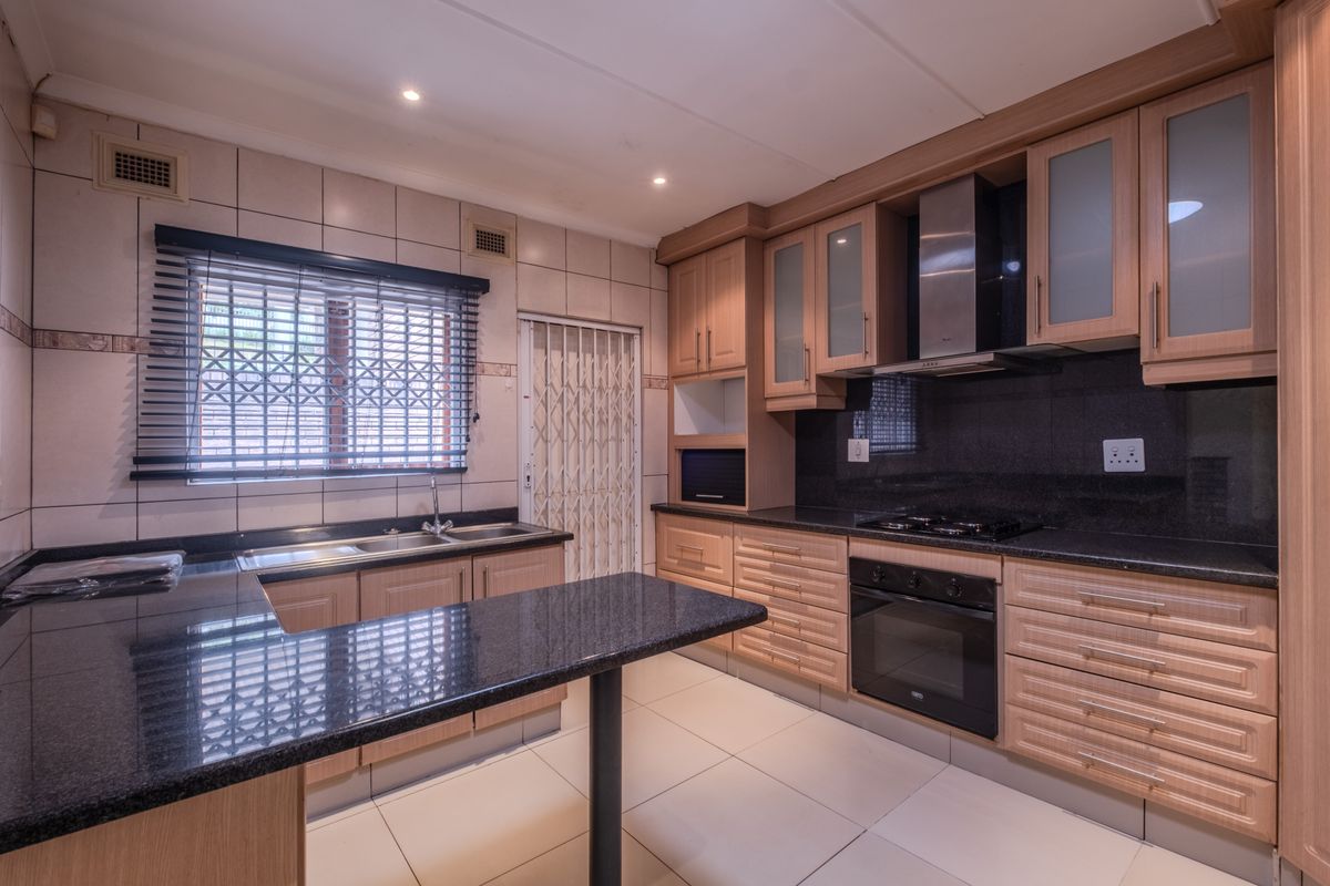 A functional kitchen featuring granite countertops, built-in oven, gas hob, extractor fan, and ample cabinetry, finished with tiled flooring and backsplash.