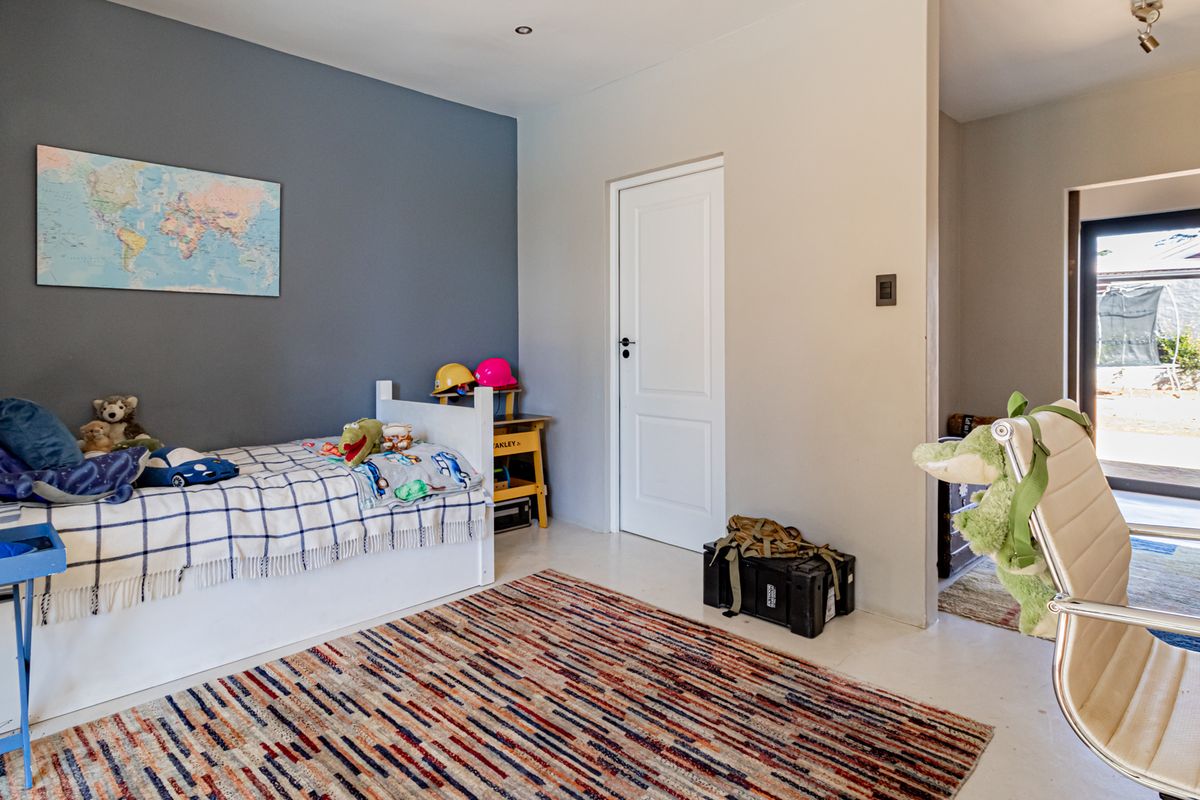 A well-lit bedroom featuring neutral tiled flooring, a feature wall, and direct access to an adjoining space with outdoor views.