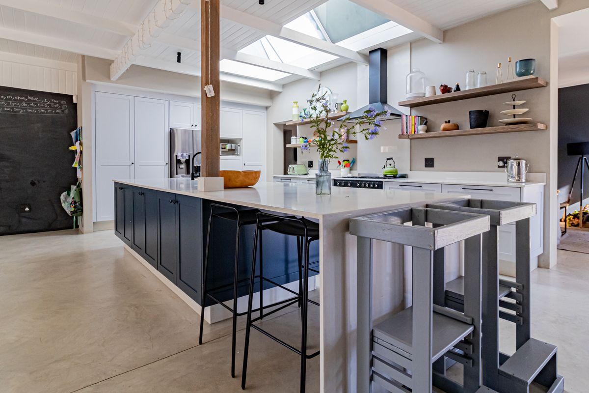 Modern open-plan kitchen featuring a large central island, sleek cabinetry, open shelving, and abundant natural light provided by overhead skylights.