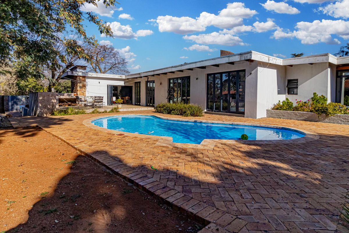 Rear exterior view featuring a swimming pool, brick paved patio area, and a built-in outdoor fireplace with direct access to the home via sliding doors.