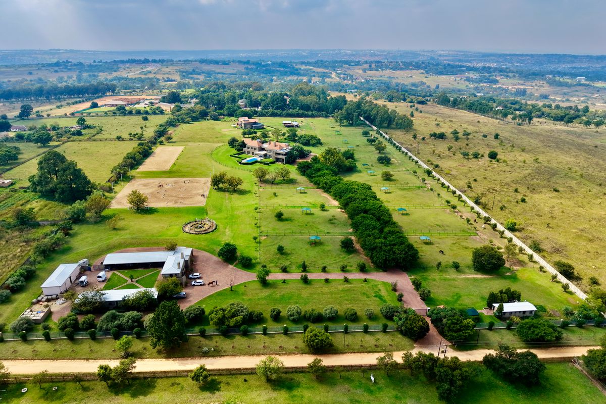 Aerial view of a large rural estate featuring a main residence, swimming pool, extensive equestrian facilities, paddocks, and landscaped grounds.