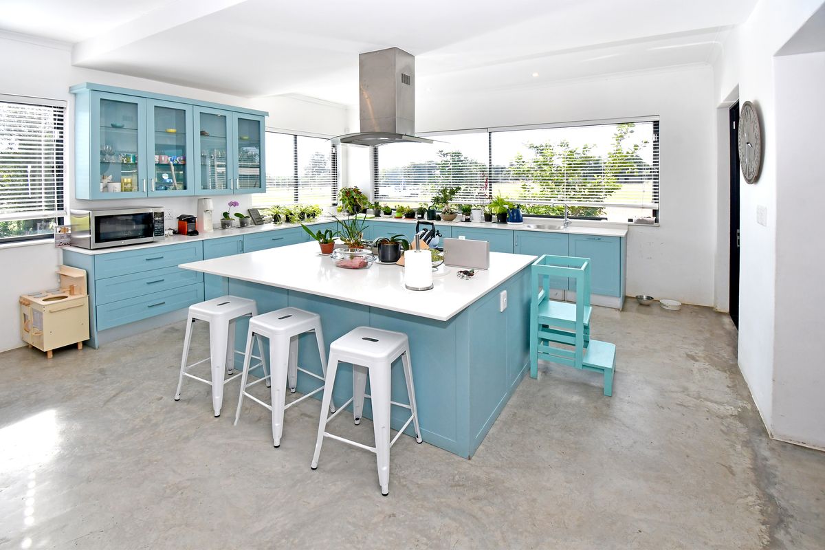 Modern kitchen featuring light blue cabinetry, a central island with stone countertops, stainless steel extractor fan, and polished concrete flooring.
