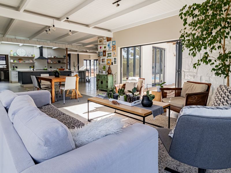Spacious open-plan living and kitchen area featuring exposed beam ceilings, polished concrete floors, a stone feature wall, and large bi-fold doors leading outdoors.