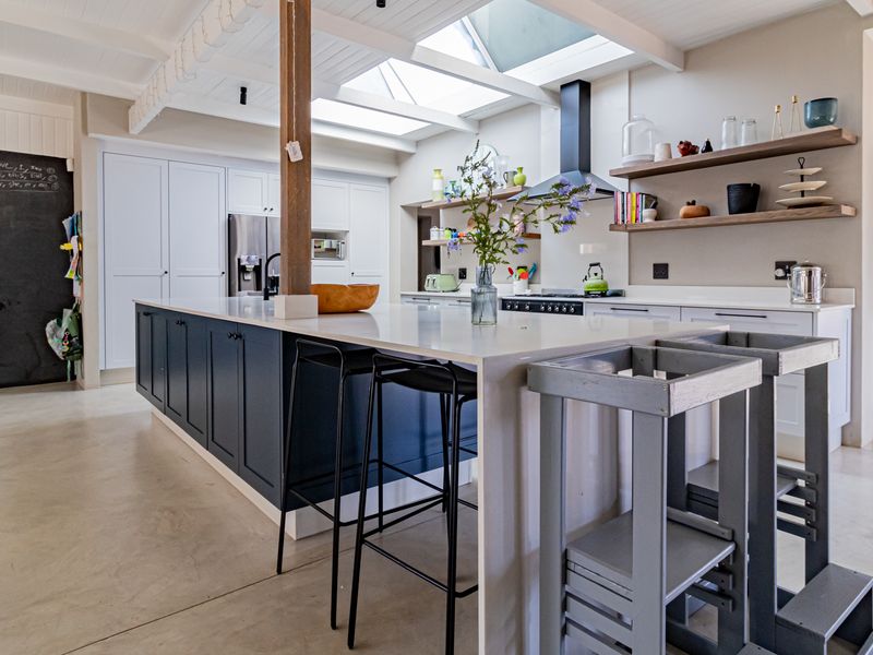Modern open-plan kitchen featuring a large central island, sleek cabinetry, open shelving, and abundant natural light provided by overhead skylights.