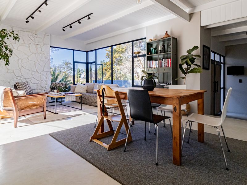 Spacious open-plan living and dining area featuring polished concrete floors, a striking stone feature wall, and expansive black-framed windows with natural light.