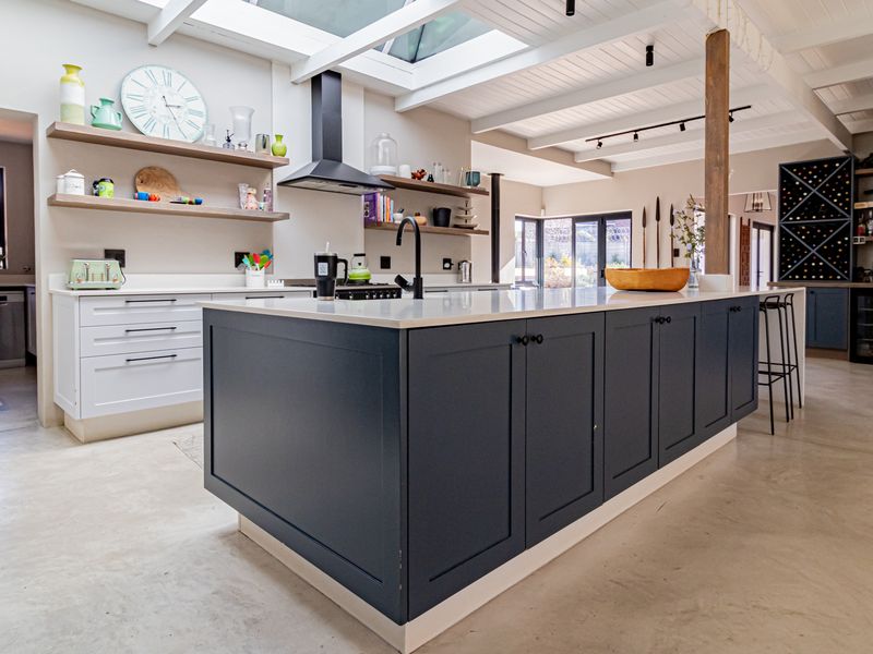 Modern open-plan kitchen featuring a large central island, quartz countertops, skylights, exposed timber beams, and polished concrete floors with integrated wine storage.