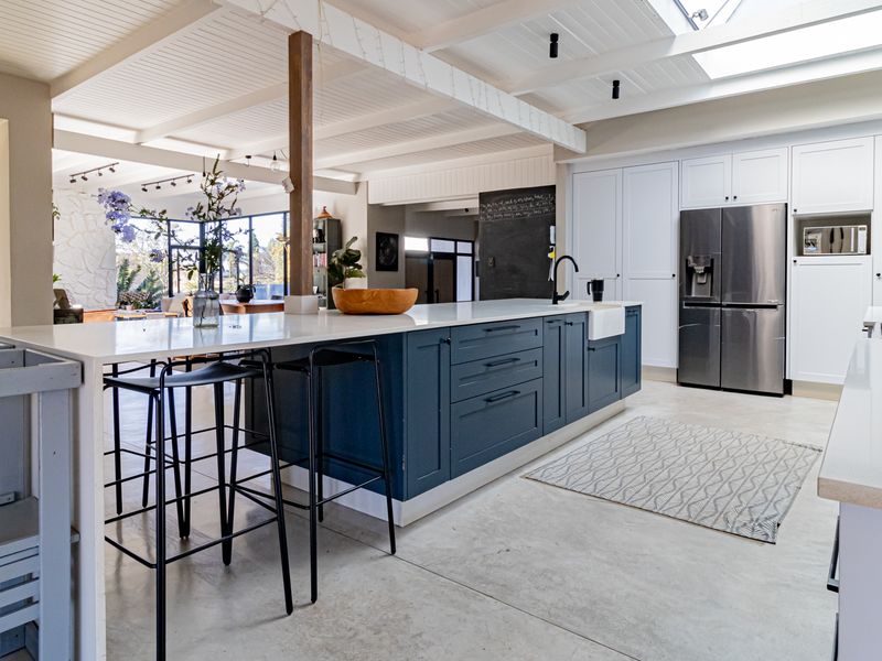 Modern open-plan kitchen featuring a large central island, farmhouse sink, sleek cabinetry, exposed beam ceiling with skylights, and polished concrete flooring.