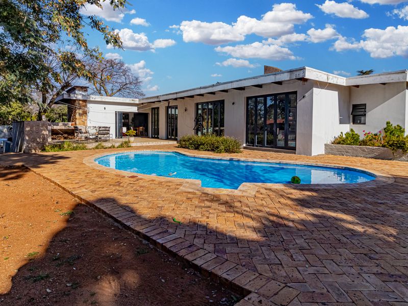 Rear exterior view featuring a swimming pool, brick paved patio area, and a built-in outdoor fireplace with direct access to the home via sliding doors.