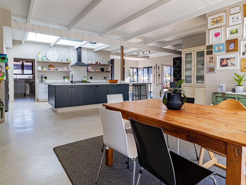 Spacious open-plan living and dining area featuring a modern kitchen with a central island, skylights, exposed beams, and polished concrete floors.