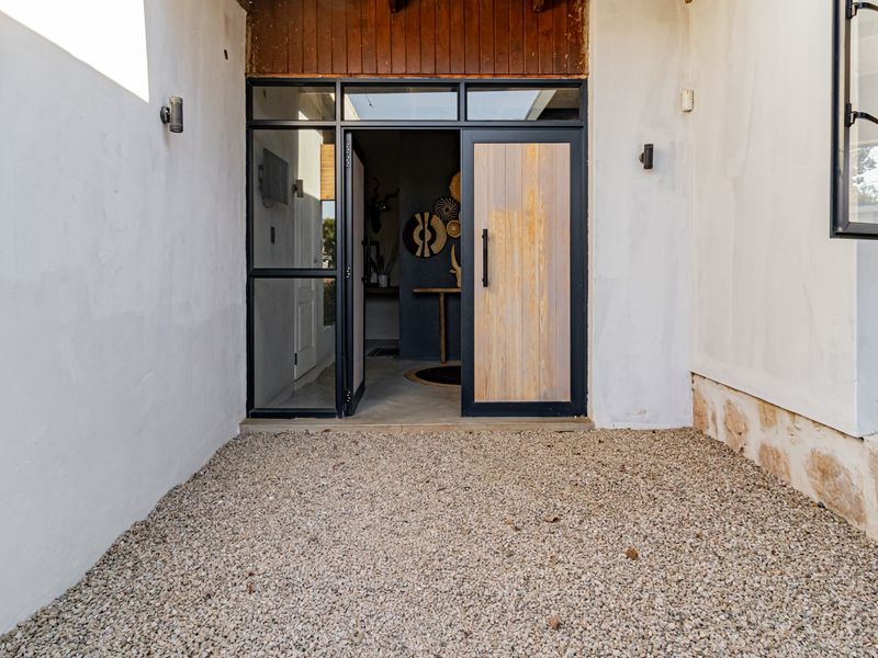 A modern entrance featuring a timber and glass pivot door, stone base detailing, and a gravel courtyard area.