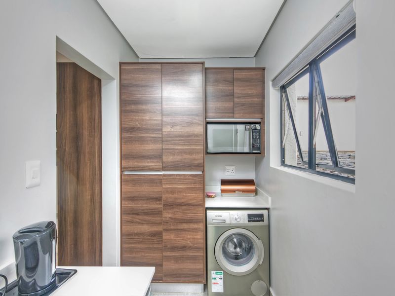 A compact, well-organized laundry area featuring modern wood-finish cabinetry, a built-in microwave, and space for a washing machine under a solid countertop.