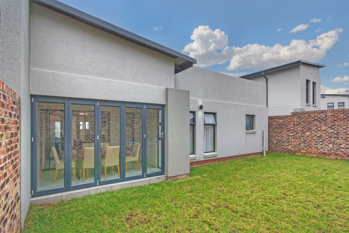 Rear view of the townhouse featuring a private garden, brick boundary walls, and modern bi-fold glass doors leading into the interior living space.