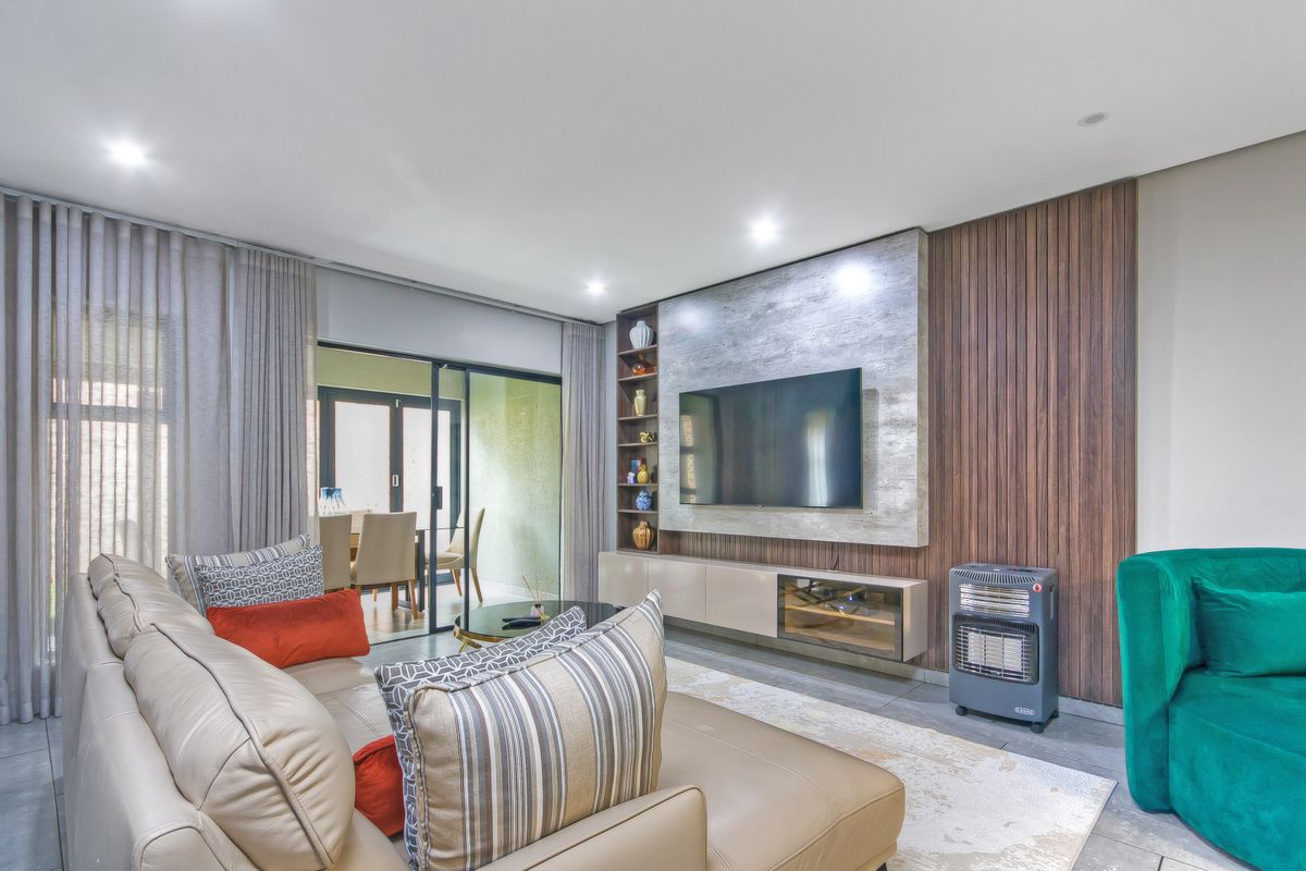 Modern living room featuring a custom built-in media unit with timber slat paneling, recessed lighting, and large sliding doors leading to an outdoor area.