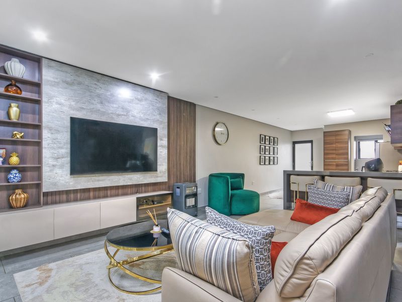 Modern open-plan living area featuring a custom media wall with integrated shelving and a sleek kitchen with a breakfast bar.