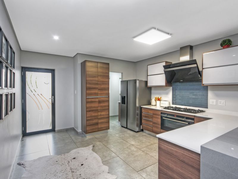 Modern kitchen featuring wood-grain cabinetry, stone countertops, gas hob, extractor fan, and tiled flooring with direct access to an adjacent utility area.