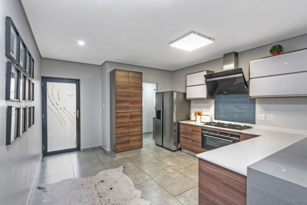 Modern kitchen featuring wood-grain cabinetry, stone countertops, gas hob, extractor fan, and tiled flooring with direct access to an adjacent utility area.