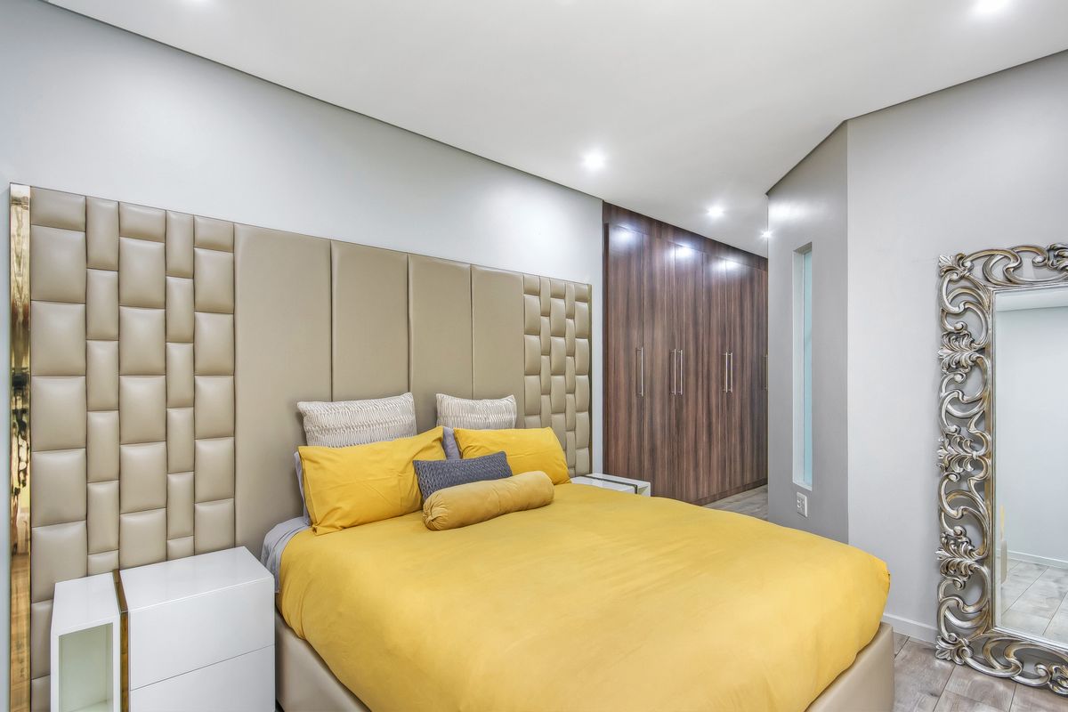 Modern bedroom featuring a large upholstered headboard, extensive built-in wooden cabinetry, recessed lighting, and sleek tiled flooring.