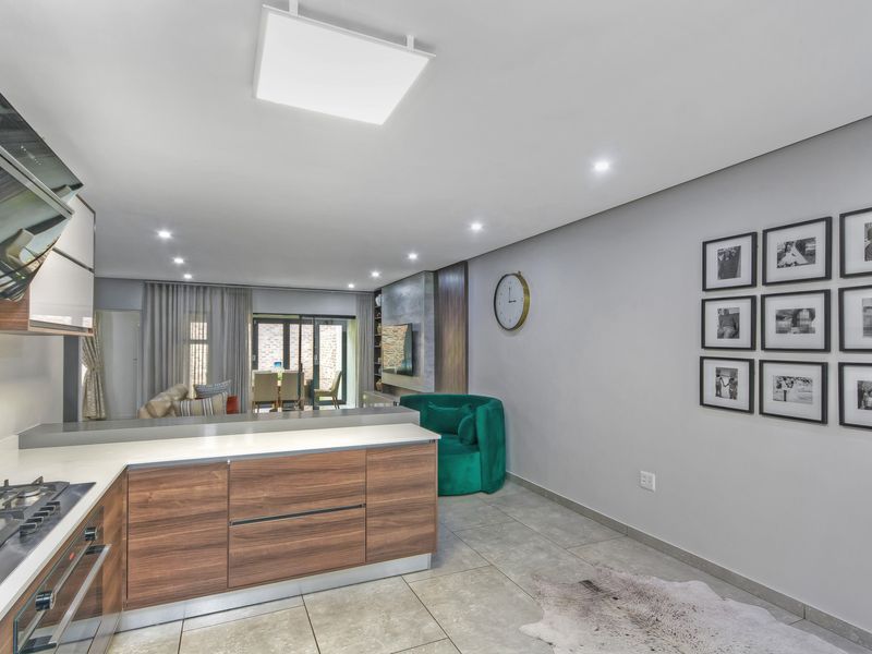 Modern open-plan kitchen and living area featuring sleek wood-finish cabinetry, stone countertops, integrated appliances, and large sliding doors leading to the outdoor space.