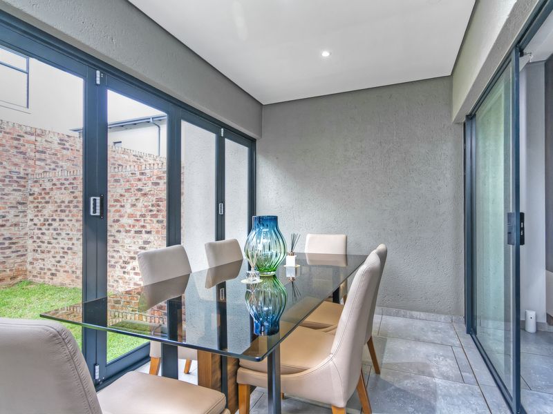 A modern covered patio featuring bi-fold glass doors, tiled flooring, recessed lighting, and a built-in shelving unit, overlooking a private garden area.