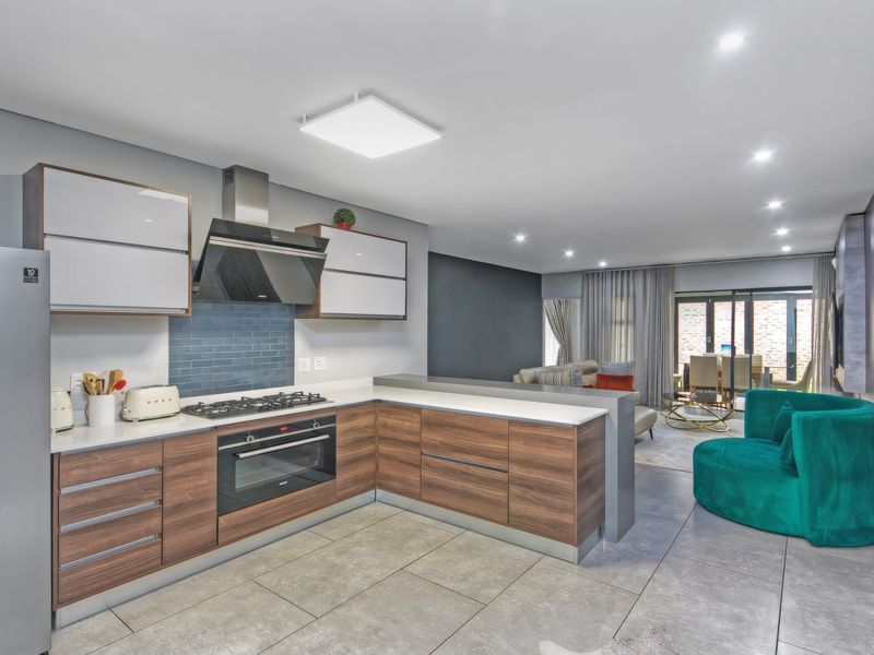 Modern open-plan kitchen and living area featuring contemporary cabinetry, high-end built-in appliances, stone countertops, and large format floor tiles.