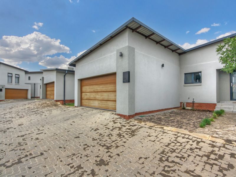 Modern townhouse exterior featuring a paved driveway, sectional wooden garage door, and clean stucco facade with brick detailing.