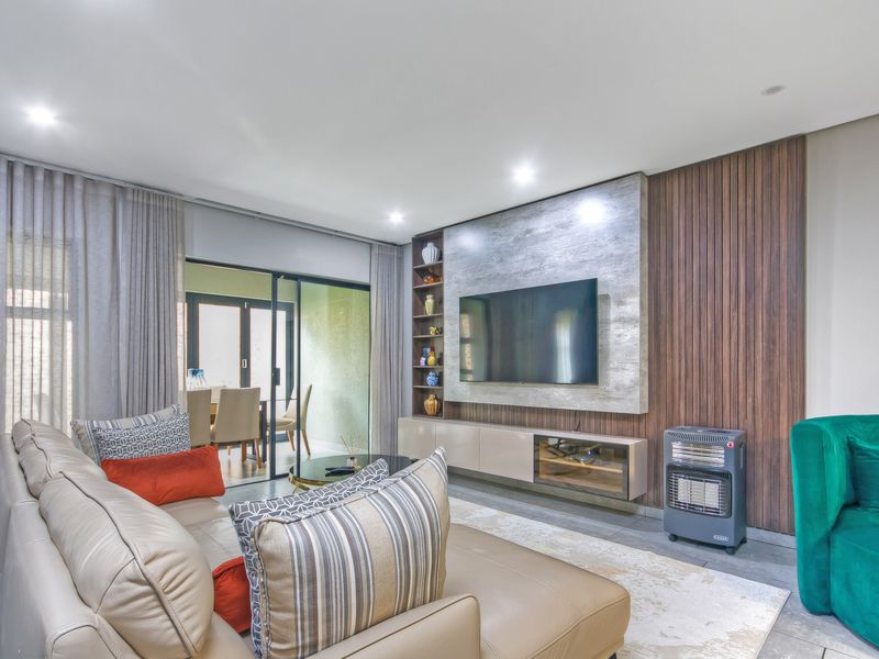 Modern living room featuring a custom built-in media unit with timber slat paneling, recessed lighting, and large sliding doors leading to an outdoor area.