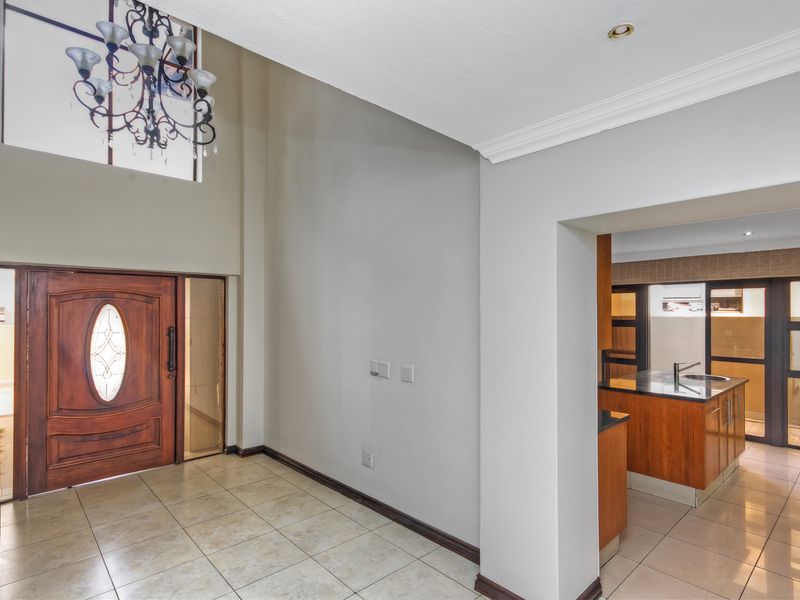 Spacious double-volume entrance hall featuring tiled flooring, a decorative chandelier, and a solid wood front door, leading through to the kitchen area.