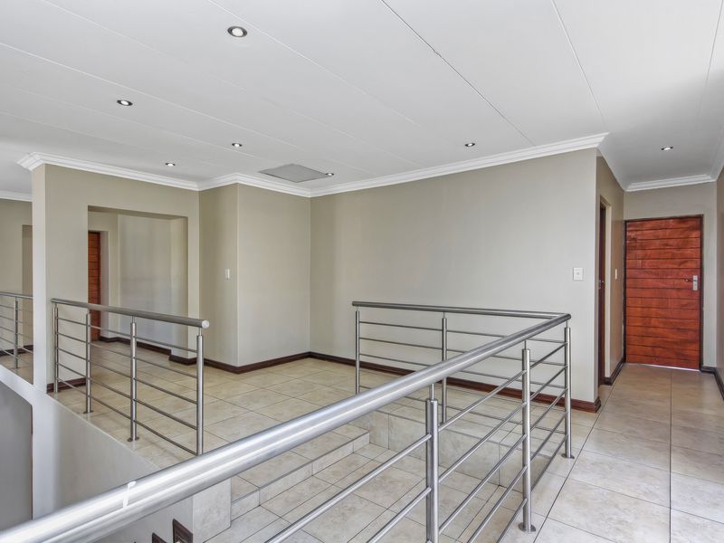 A spacious, well-lit landing area featuring modern stainless steel balustrades, neutral tiled flooring, and recessed ceiling lighting.