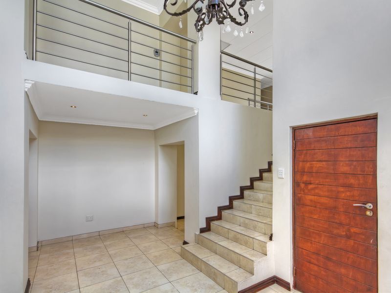 Spacious double-volume entrance hall featuring tiled flooring, a staircase with stainless steel balustrades, and a mezzanine landing overlooking the foyer.