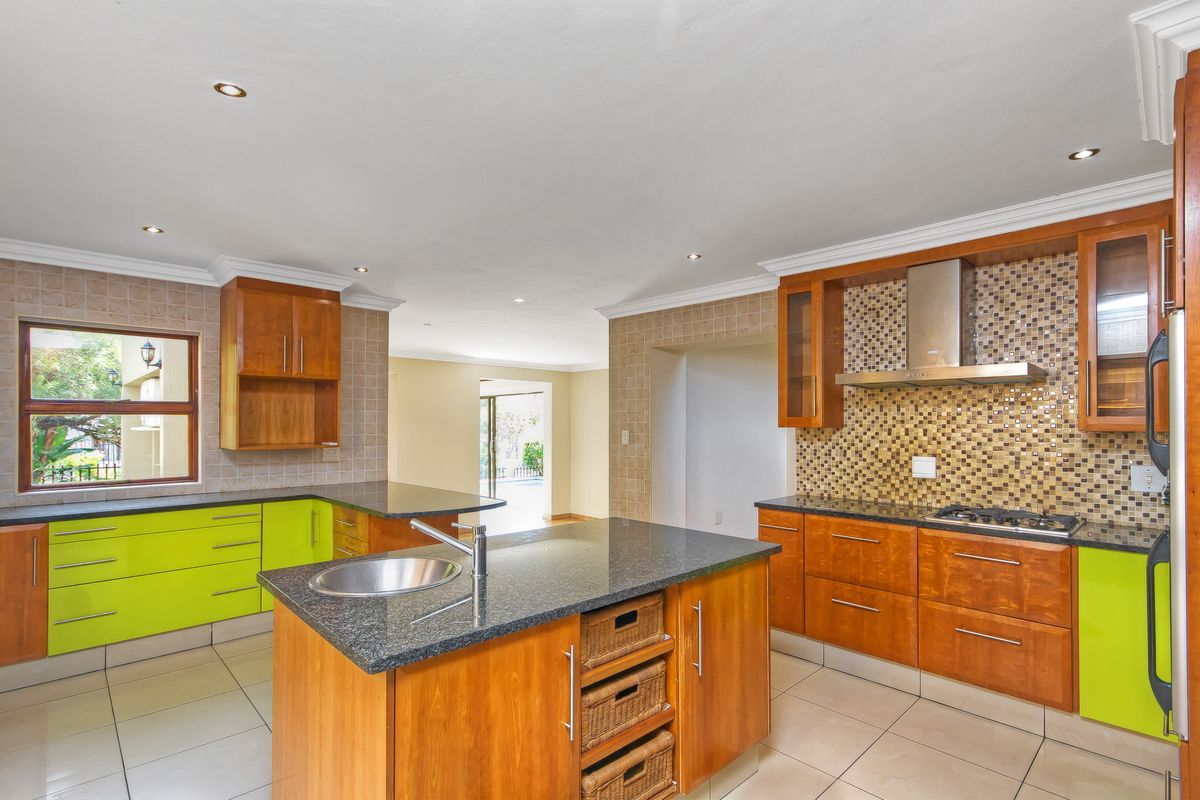 Spacious kitchen featuring a central island with sink, granite countertops, gas hob, stainless steel extractor, and a mix of wood and lime green cabinetry.