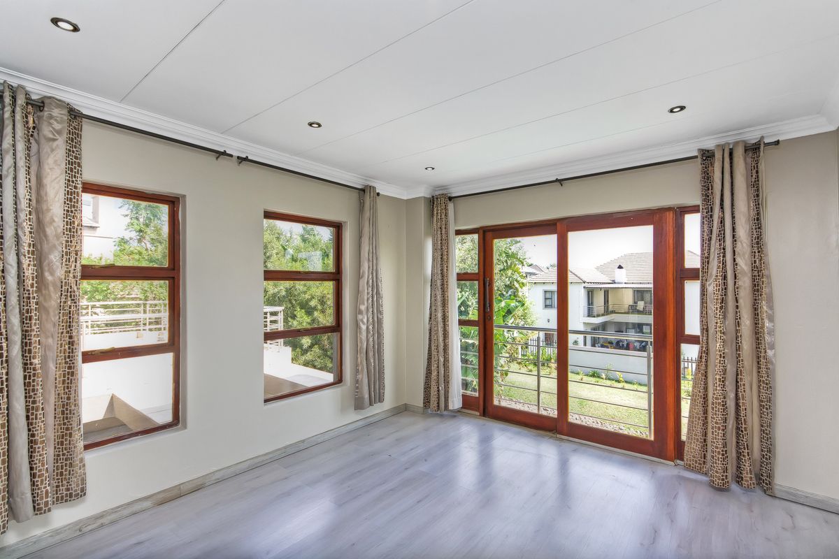 Bright and spacious living area featuring modern laminate flooring, recessed downlights, and large timber-framed windows and sliding doors leading to an outdoor balcony.