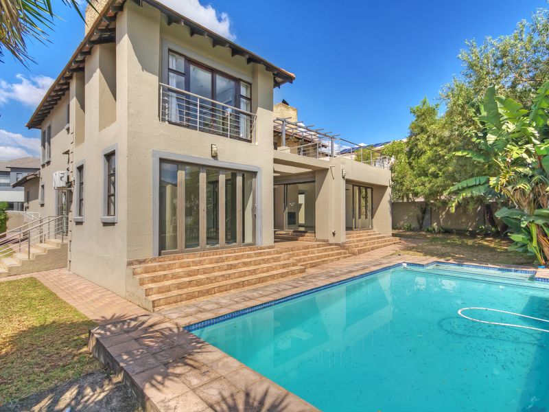 Rear exterior view of a multi-story house featuring a swimming pool, tiled patio area, and upper-level balcony with stainless steel balustrades.