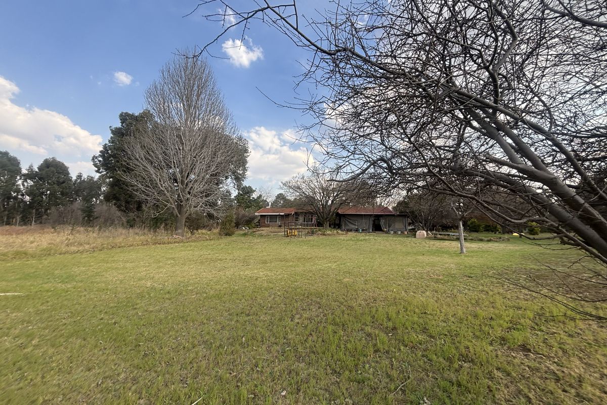 A wide-angle view of a residential property featuring a large grassy yard, mature trees, and the rear elevation of the dwelling.