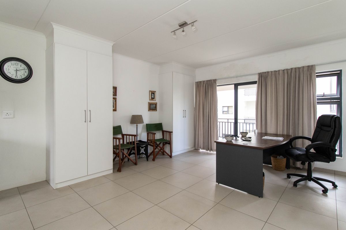 A bright bedroom featuring neutral tiled flooring, ample built-in cupboard storage, and a sliding door providing access to an outdoor balcony area.