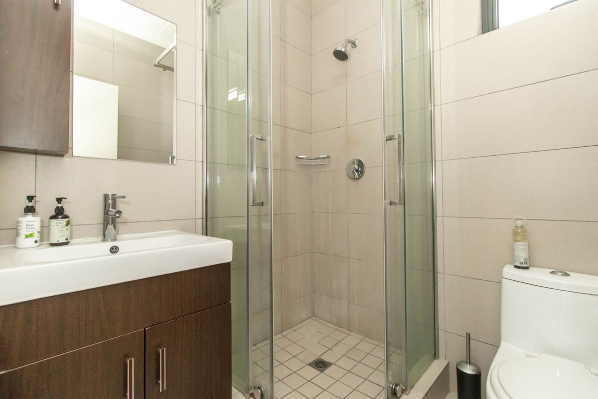 A modern bathroom featuring a vanity cabinet with basin, a glass-enclosed shower, and neutral wall tiling.