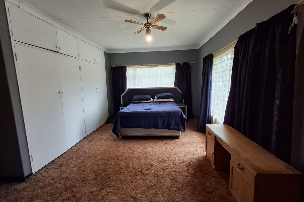 Spacious bedroom featuring extensive built-in cupboards, a ceiling fan, and large windows, offering a functional layout with potential for modern updates.