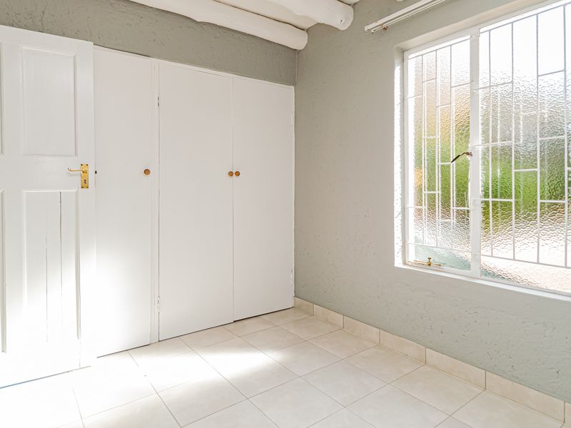 A bright, empty bedroom featuring built-in cupboards, tiled flooring, and exposed ceiling beams, offering a clean canvas for personalization.