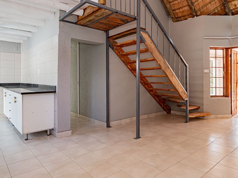 Open plan living area featuring a kitchen with stone countertops, tiled floors, exposed timber beams, and a staircase leading to an upper level.