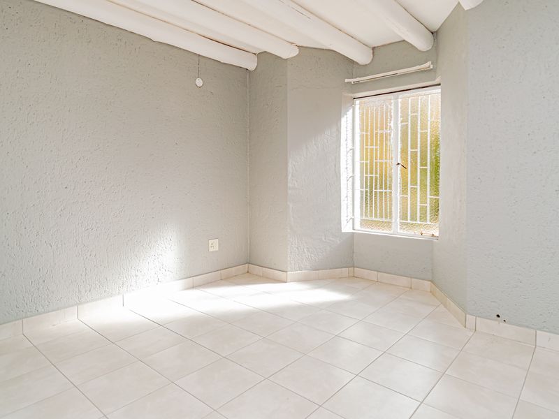 An empty bedroom featuring tiled flooring, exposed ceiling beams, and a window fitted with security bars.