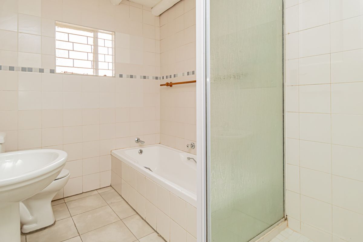 A functional bathroom featuring a pedestal basin, a built-in bathtub, and a separate shower enclosure with tiled walls and flooring.
