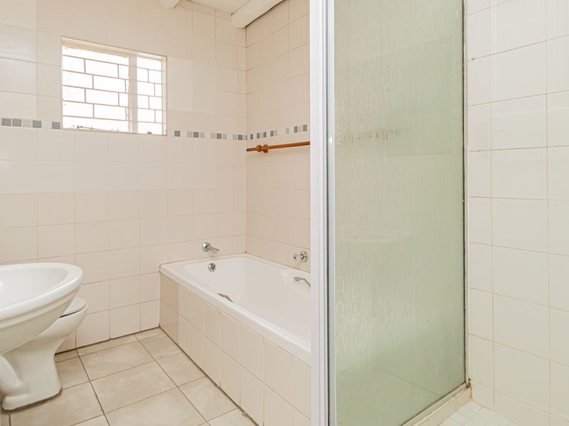 A functional bathroom featuring a pedestal basin, a built-in bathtub, and a separate shower enclosure with tiled walls and flooring.
