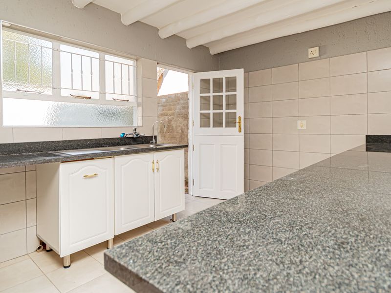 A functional kitchen featuring granite countertops, a stainless steel sink, tiled walls, and exposed beam ceilings, offering a clean and practical workspace.