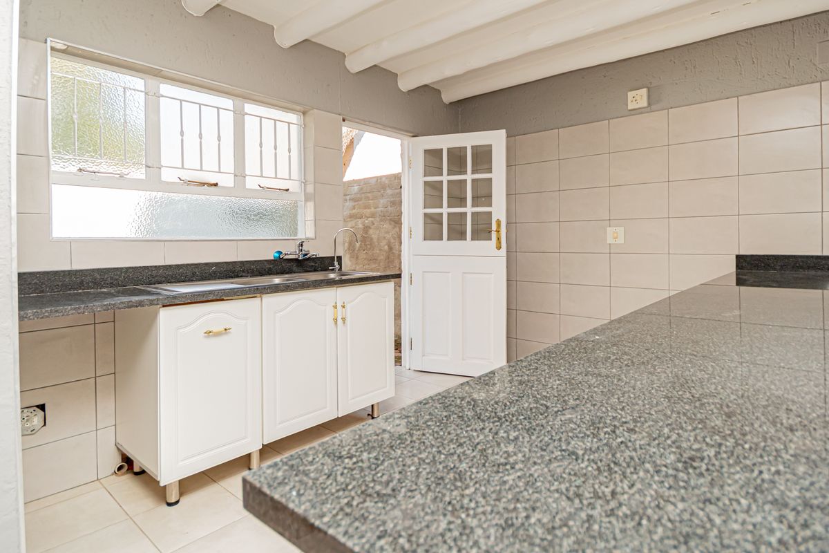 A functional kitchen featuring granite countertops, a stainless steel sink, tiled walls, and exposed beam ceilings, offering a clean and practical workspace.