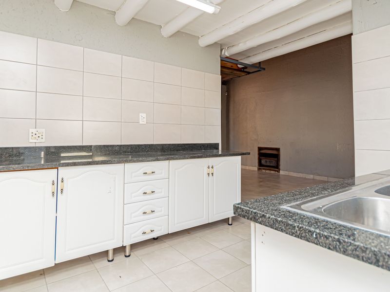 A functional kitchen space featuring granite countertops, white cabinetry, and a stainless steel sink, with exposed ceiling beams and neutral tiled flooring.