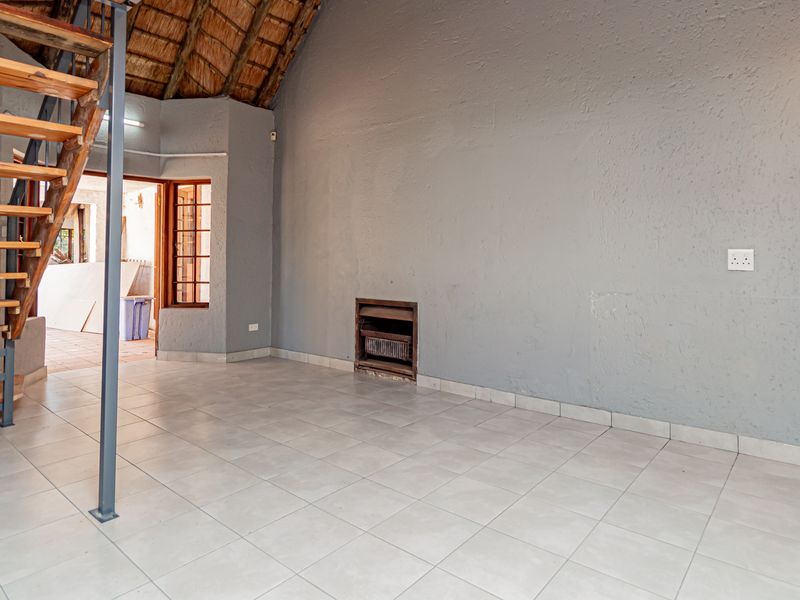 Spacious living area featuring a unique thatched roof, built-in fireplace, and an open timber staircase, offering a rustic cottage aesthetic.