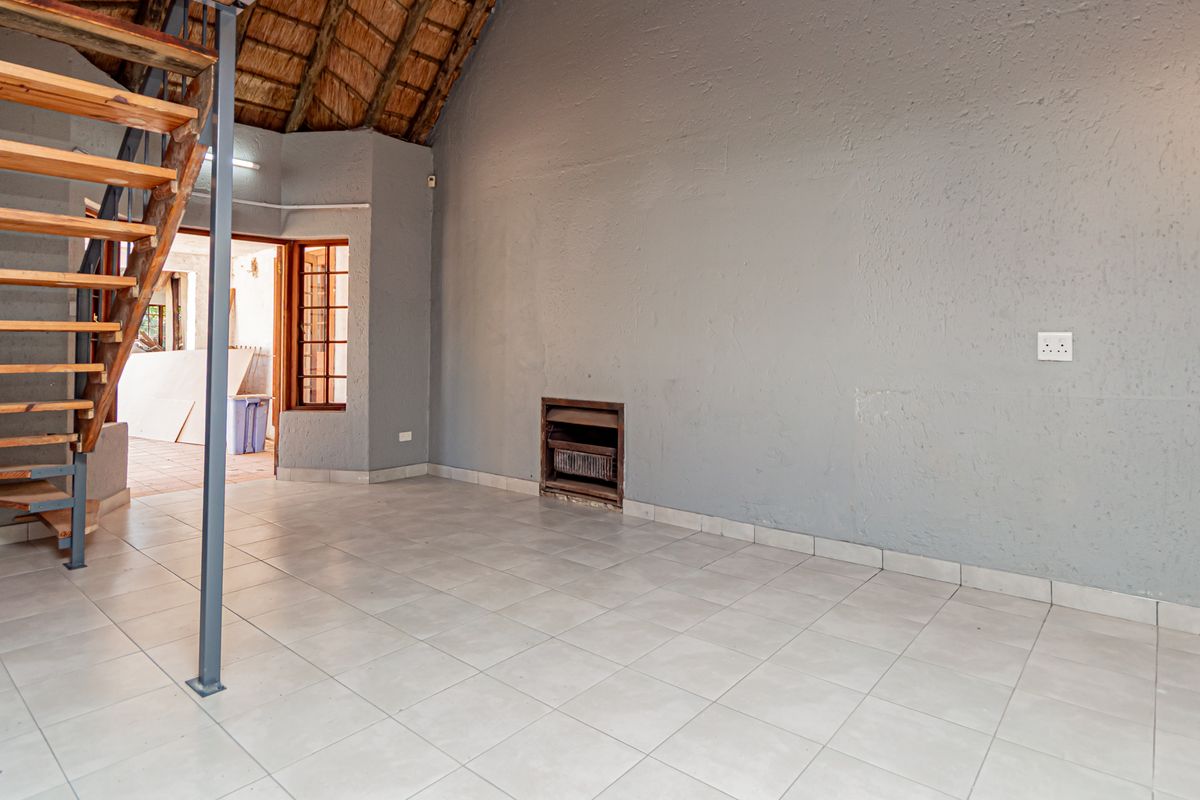Spacious living area featuring a unique thatched roof, built-in fireplace, and an open timber staircase, offering a rustic cottage aesthetic.