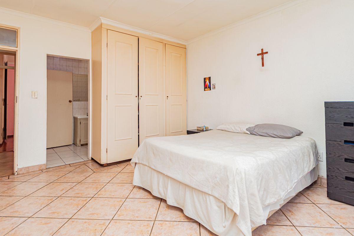 A bedroom featuring tiled flooring, built-in cupboards, and coved cornicing, with an adjoining en-suite bathroom visible through the doorway.