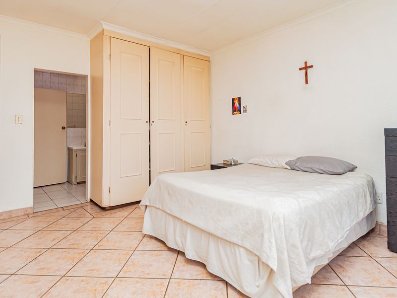 A bedroom featuring tiled flooring, built-in cupboards, and coved cornicing, with an adjoining en-suite bathroom visible through the doorway.